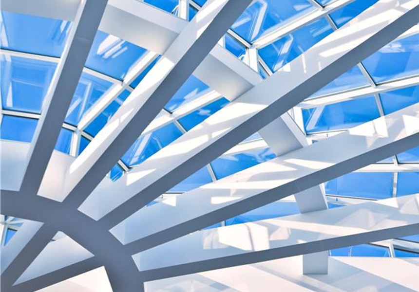 Modern architectural ceiling with intersecting white beams and large glass panels with a bright blue sky above.
